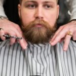 A stylish bearded man receiving precision grooming at a barbershop.